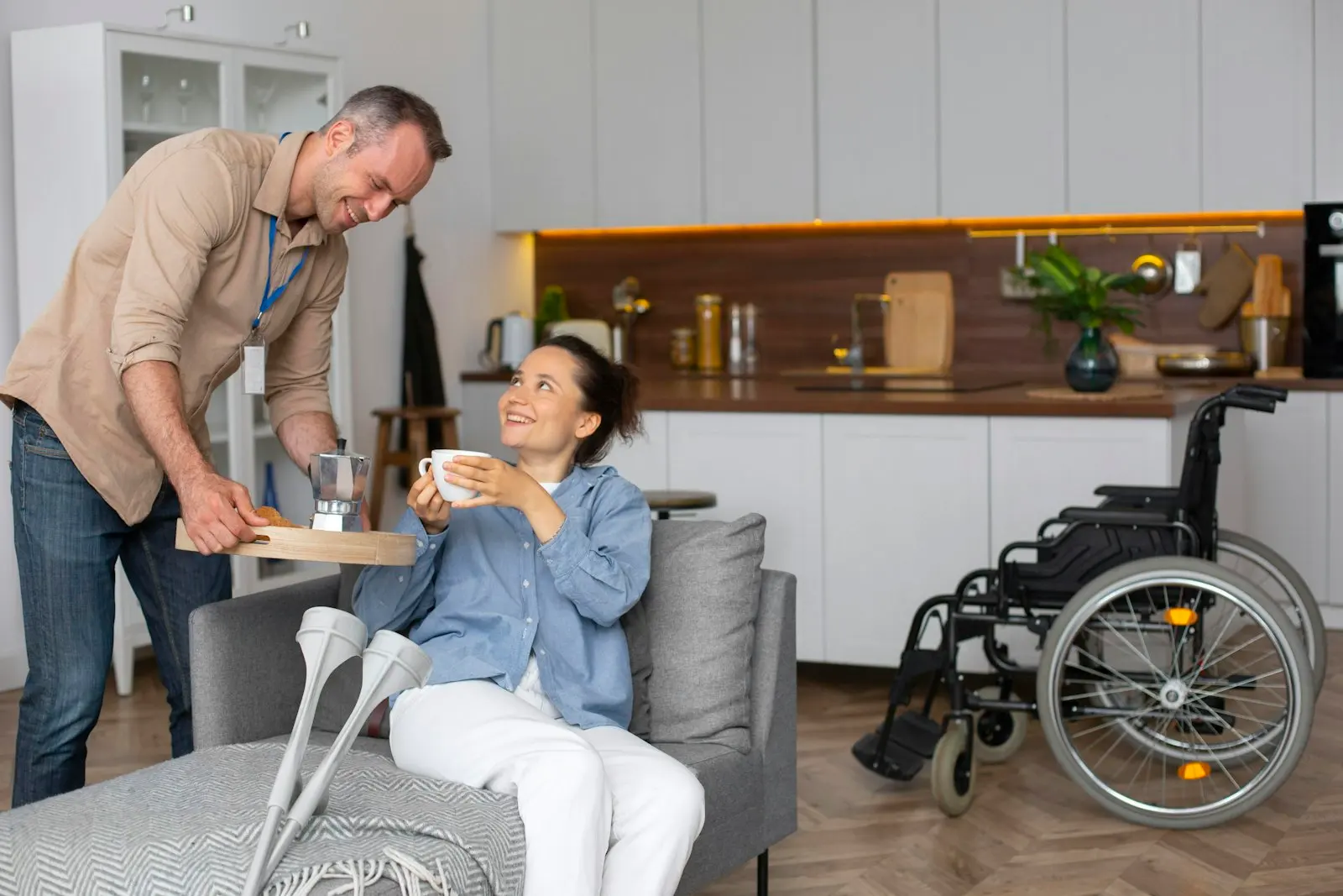 A helper bringing a cup of tea to a woman resting at home, her wheelchair beside her