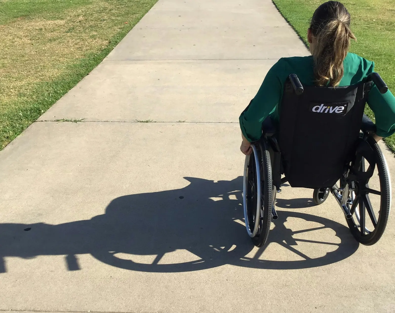 A woman in a wheelchair rolling along a sunny sidewalk
