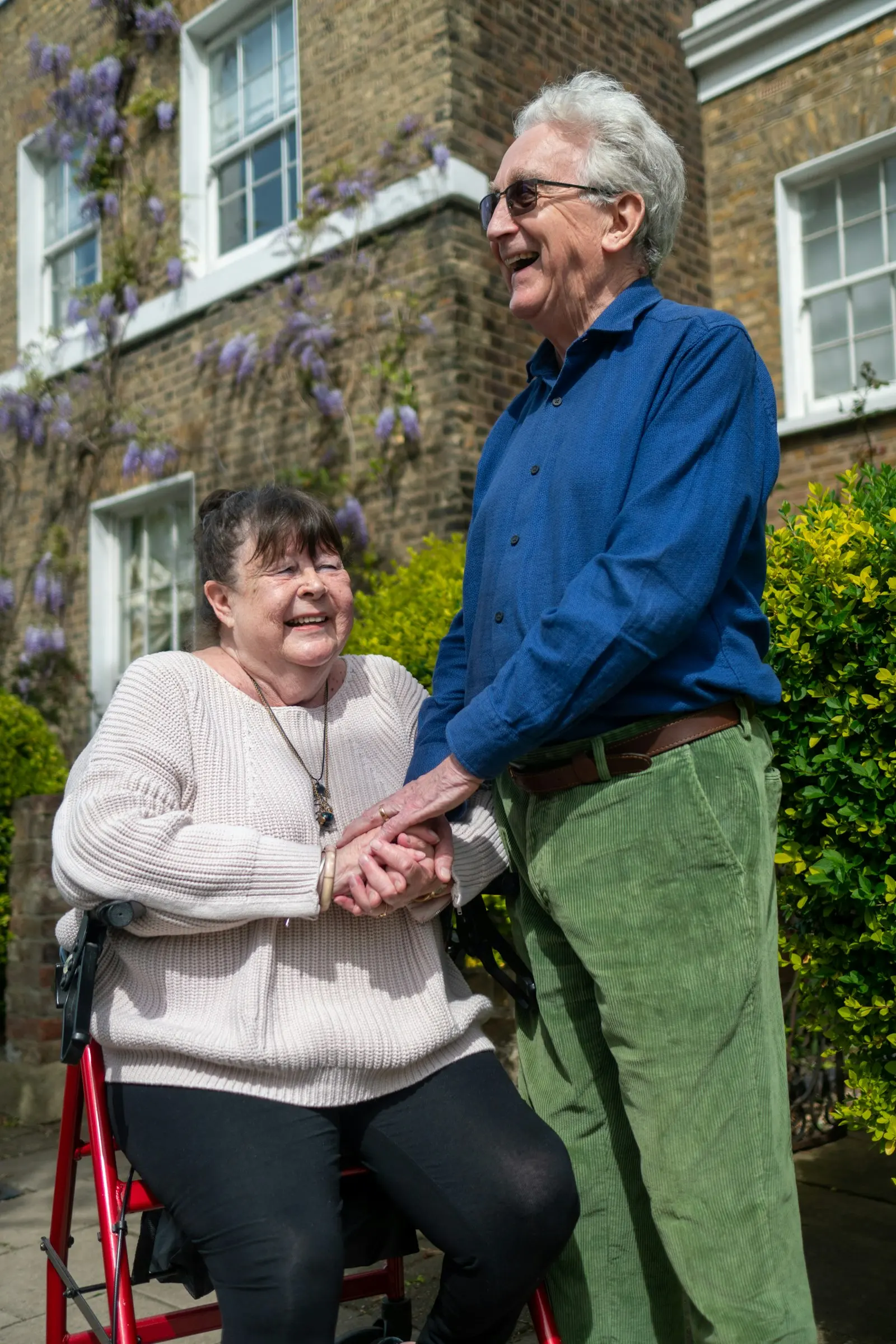 An older woman laughing as she holds hands with the person helping her outside her home