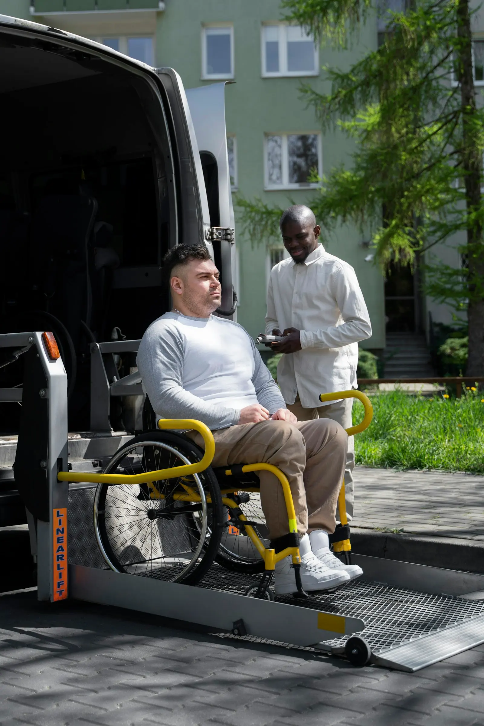 A rider in a wheelchair on a van lift, with the driver beside him ready to help